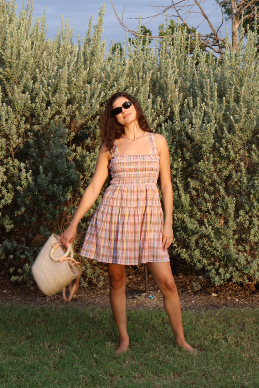 Woman in a plaid dress standing next to a bush with a clear blue sky in the background