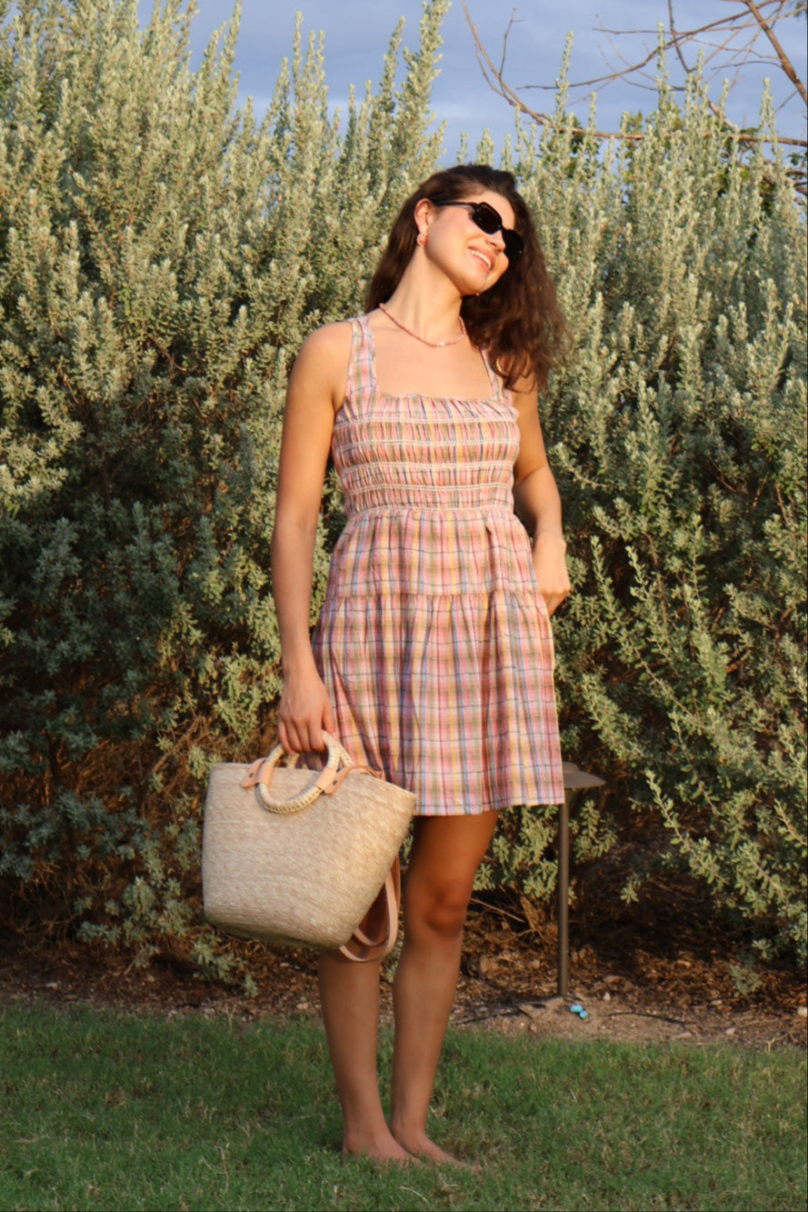 Woman in a plaid dress standing next to a tree with a clear blue sky.