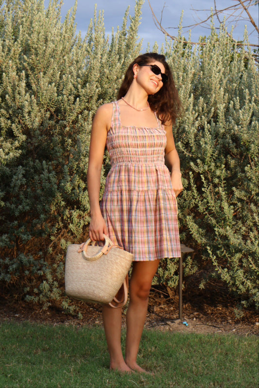 Woman in a plaid dress standing next to a tree with a clear blue sky.